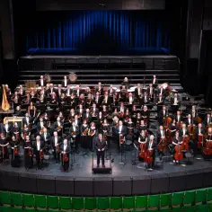 Orkiestra symfoniczna w pełnym składzie, gotowa do wykonania wesołego scherzo. Dyrygent stoi na podwyższeniu, a muzycy trzymają instrumenty.