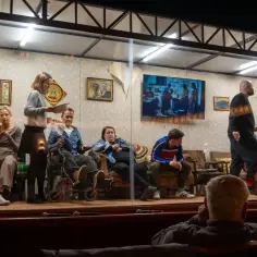 Na scenie siedzi kilka osób, w tym mężczyzna na wózku. W tle widać ekran z obrazem, jakby tkacz tworzył coś na nim.