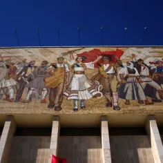 Wielki mural przedstawiający ludzi w strojach ludowych i wojskowych, symbolizujący siłę i jedność. To przykład sztuki socrealizmu, co to za styl?