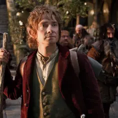 Bilbo Baggins, z charakterystyką hobbita, wyrusza w podróż. W tle widać innych hobbitów i krasnoludów.