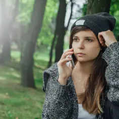 Młoda kobieta w czapce i swetrze rozmawia przez telefon w parku. Jej wyraz twarzy sugeruje, że jest cynikiem, słuchając czegoś, co ją rozczarowuje.