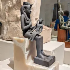 Starożytna rzeźba bogini Isis z dzieckiem na kolanach, symbolizująca macierzyństwo i opiekę.