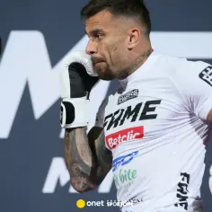 Arek Tańcula w białej koszulce FAME MMA podczas treningu, w rękawicach bokserskich, z tatuażami na ramieniu.