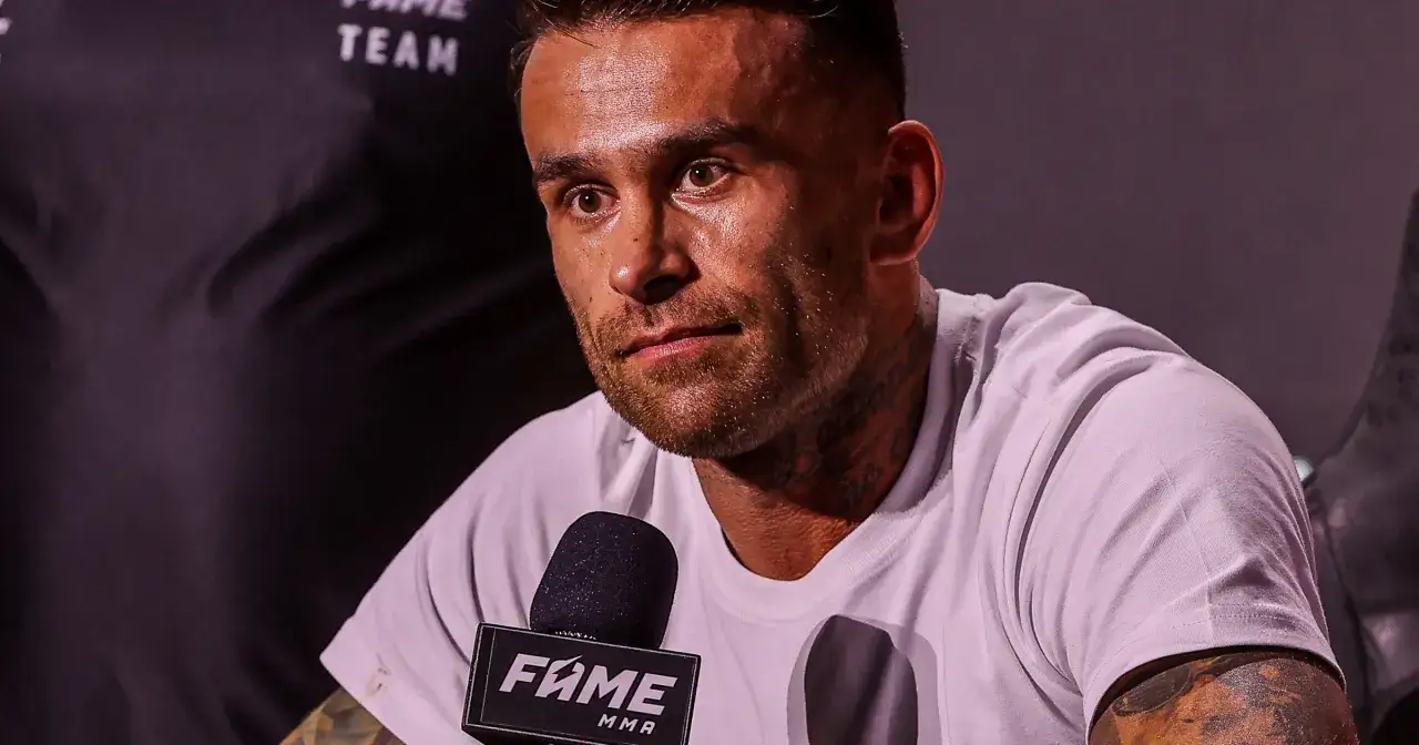 Twarz Arka Tańculi z tatuażami na szyi, w białej koszulce, przed mikrofonem FAME MMA.