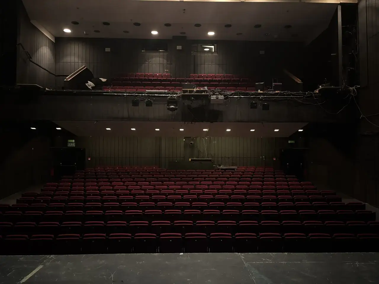 Pusta sala teatralna z rzędami czerwonych foteli. Na scenie widać sprzęt i kable, jakby przygotowywano się do akcji dywersyjnych.