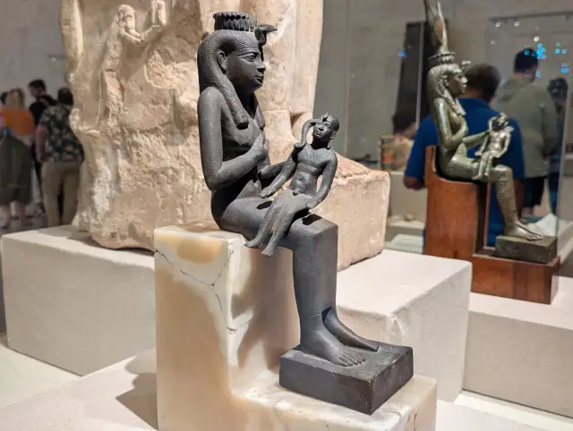 Starożytna rzeźba bogini Isis z dzieckiem na kolanach, symbolizująca macierzyństwo i opiekę.